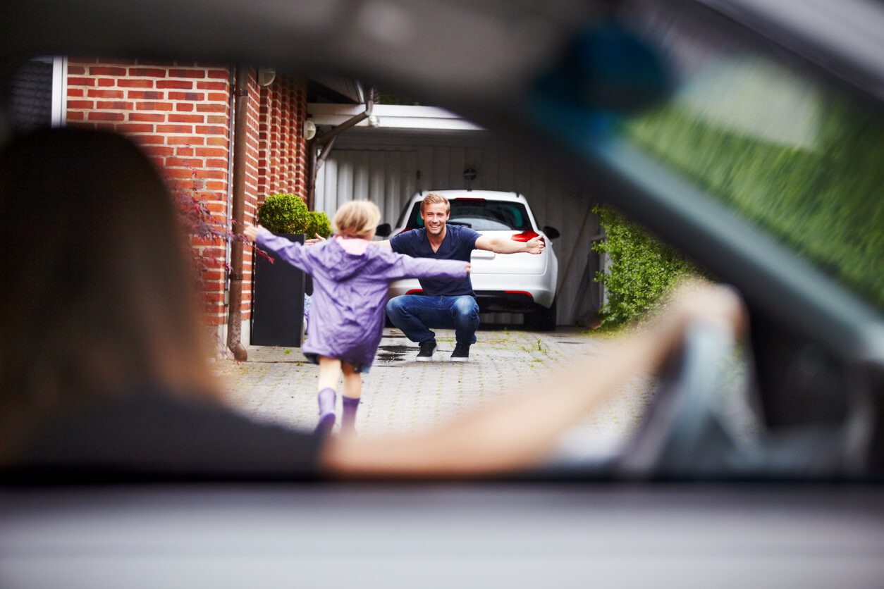 A young girl running out of her moms car excitedly to go hug her dad