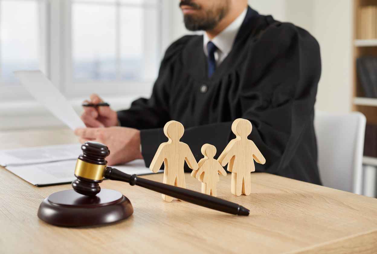 Gavel and little family figures on table in courtroom, with judge sitting in background